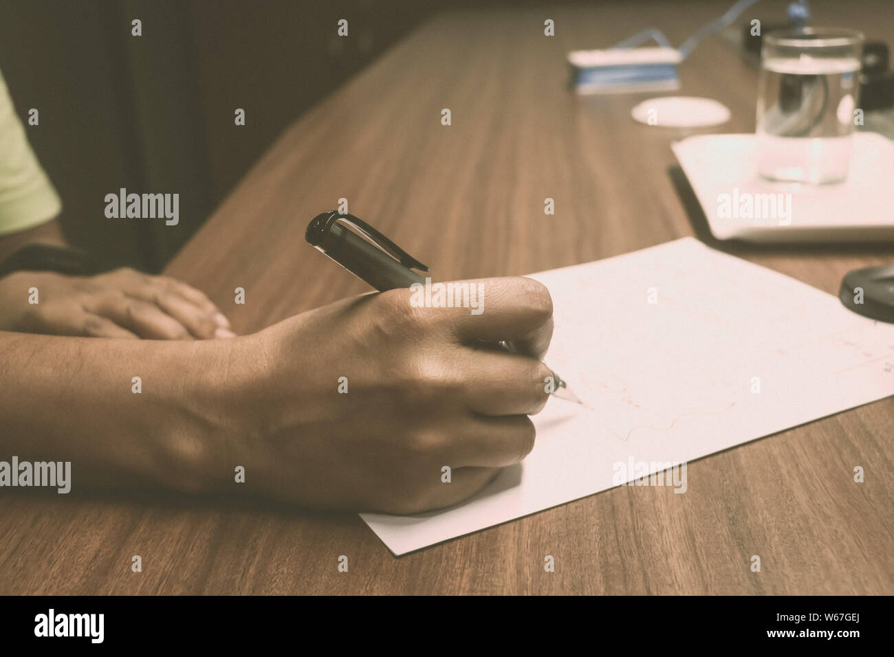 Vue de côté coup de mains d'un homme d'affaires écrit par plume dans une feuille de papier au bureau. Businessman working on table en bois. Close-up. Vinta Banque D'Images