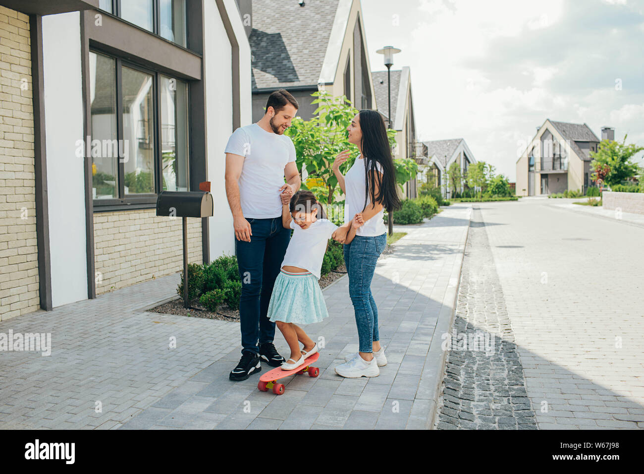 Famille heureuse marche dans la rue, leur enfant monte un skateboard Banque D'Images