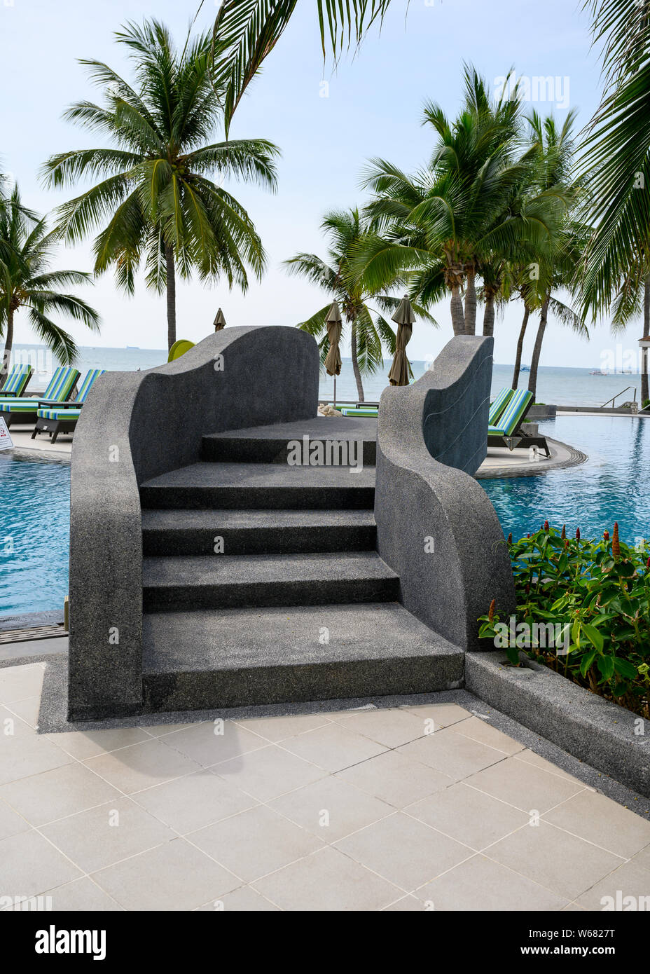 Pont noir incurvé avec escalier sur la piscine dans le jardin de palmiers sur la côte Banque D'Images