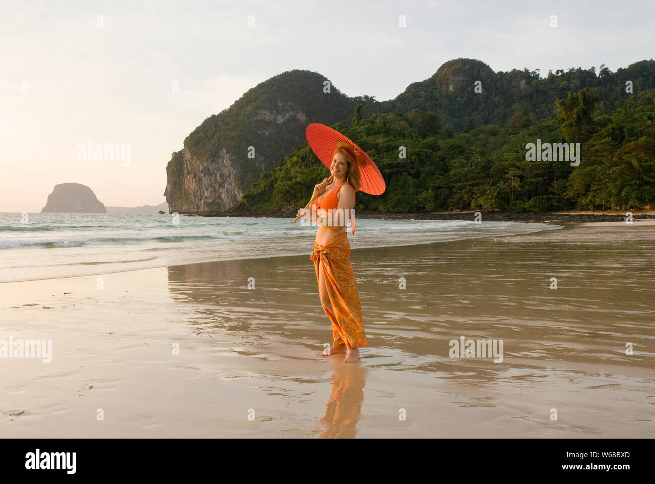 Une femme d'âge moyen en tourisme un sarong traditionnel avec un parapluie Thi debout sur une plage dans les îles Phi Phi en Thaïlande et le modèle est libéré. Banque D'Images