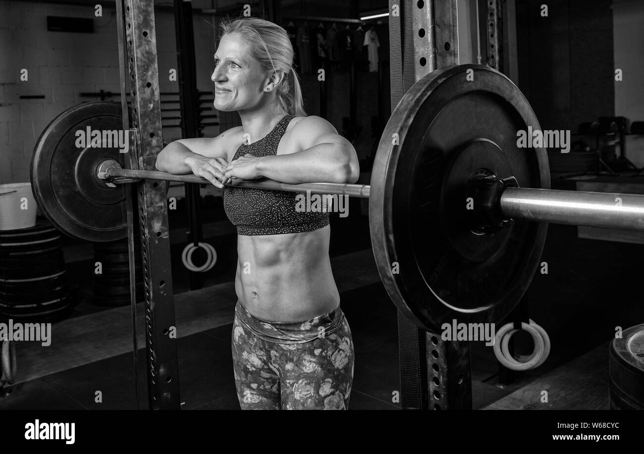Portrait noir et blanc d'une belle femme avec de fortes abs. L'athletic et smiling blonde femme est appuyée contre le longs. Banque D'Images