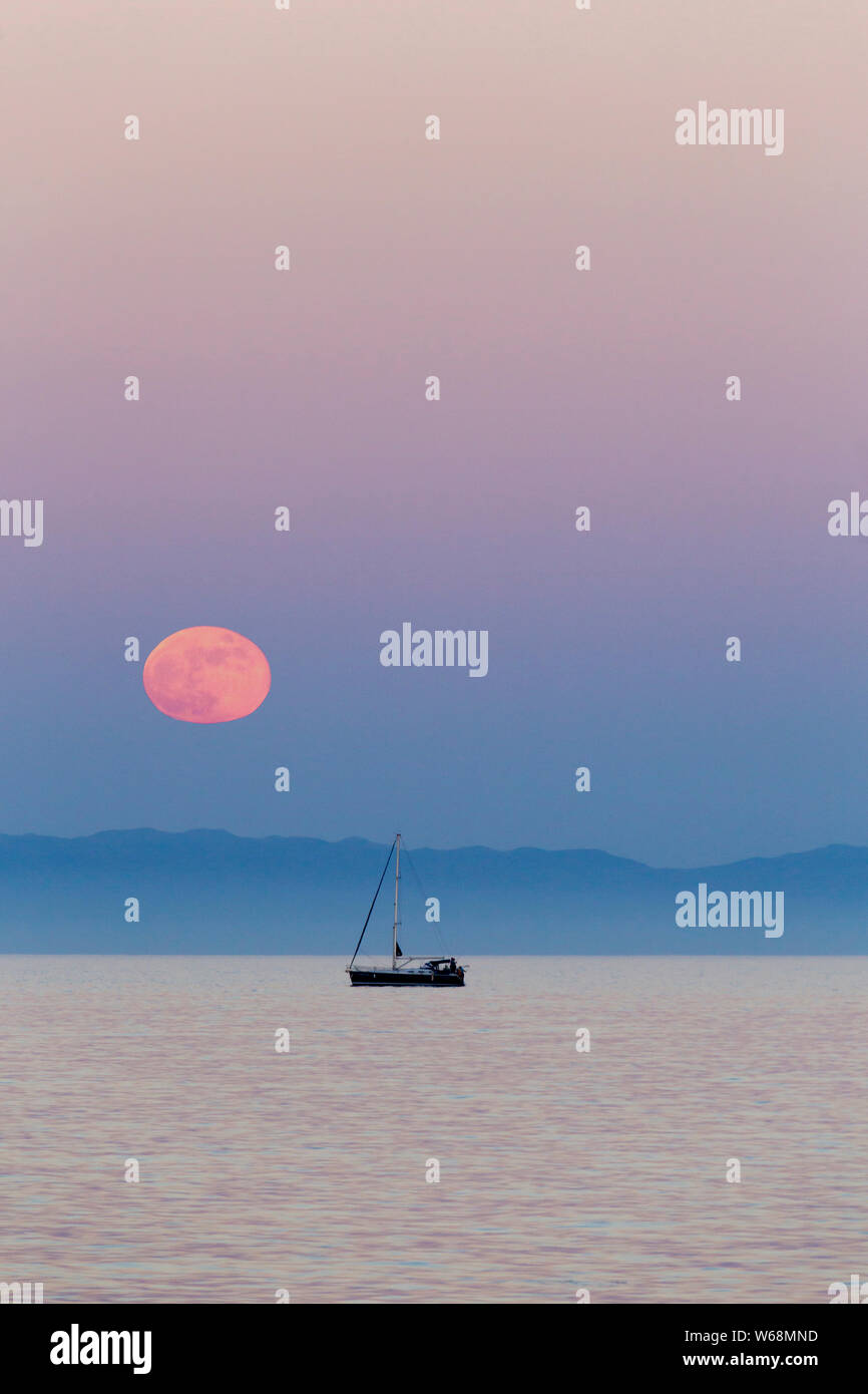 De rares Red Moon Rising sur la mer Méditerranée en Espagne avec un bateau de pêcheur à l'Horizon Banque D'Images