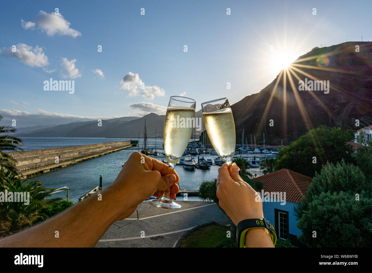 Deux mains tenant deux verres de champagne en face d'un port de plaisance pendant le coucher du soleil Banque D'Images