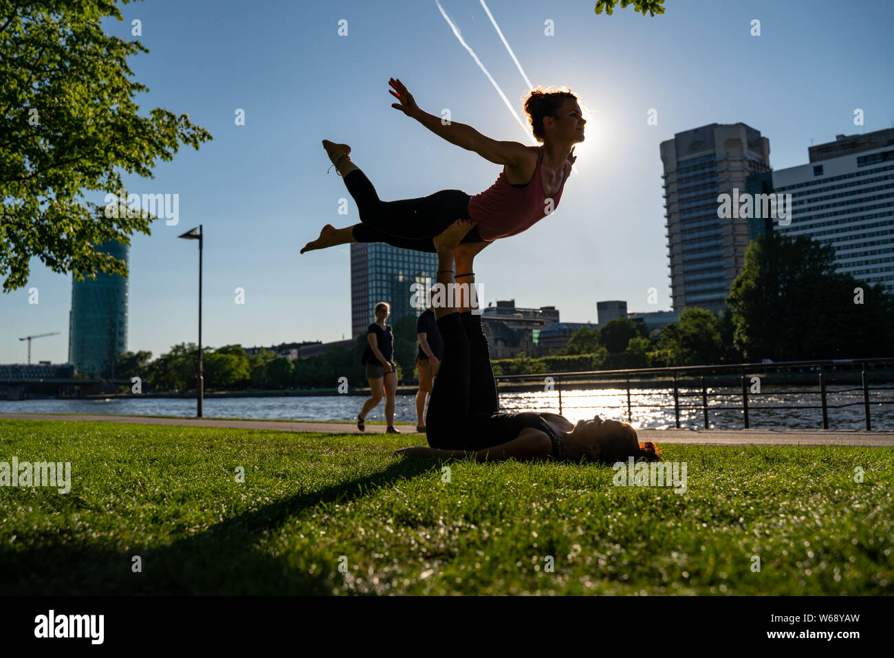 Deux jeunes filles n'acro yoga sur la rive du fleuve donnant sur la ville moderne. Jeunesse et Sport Banque D'Images