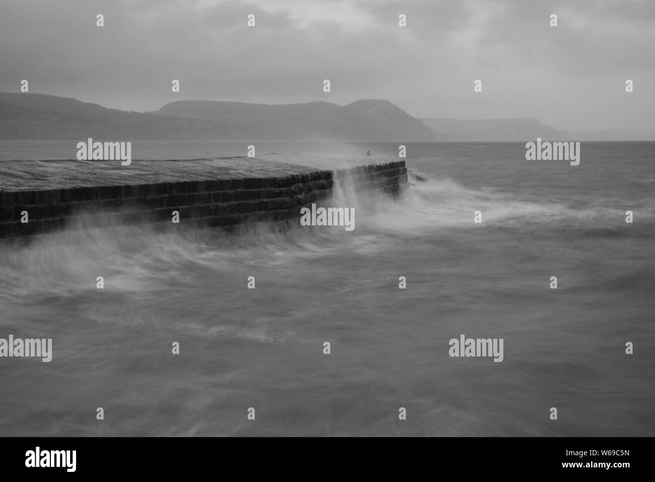 La longue exposition des vagues s'écraser contre le quai à Lyme Regis dans le Dorset en noir et blanc Banque D'Images
