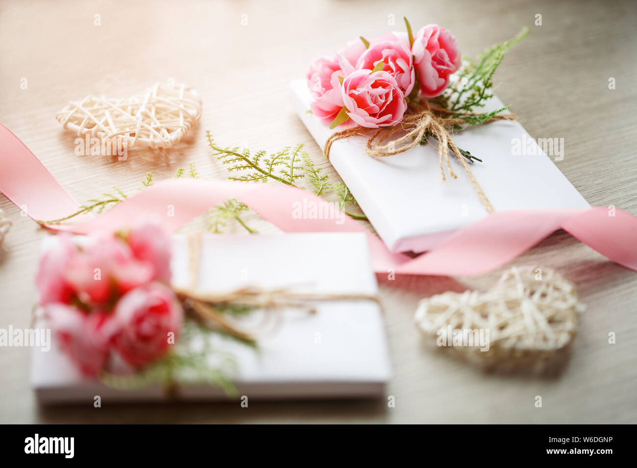 Quelques boîtes cadeau enveloppées de papier blanc artisanal simple et décorées avec un bouquet de roses et un bouquet de verts Banque D'Images