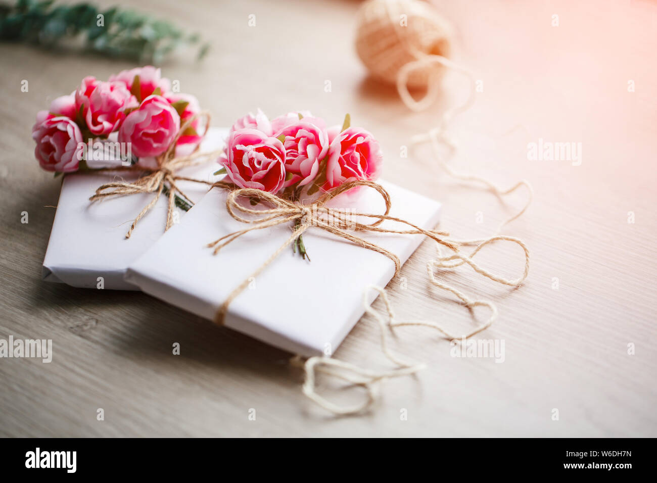 Boîte de cadeau faite à la main enveloppée de papier avec branche de roses. Branche d'eucalyptus et bobines rustiques de corde de chanvre sur fond Banque D'Images