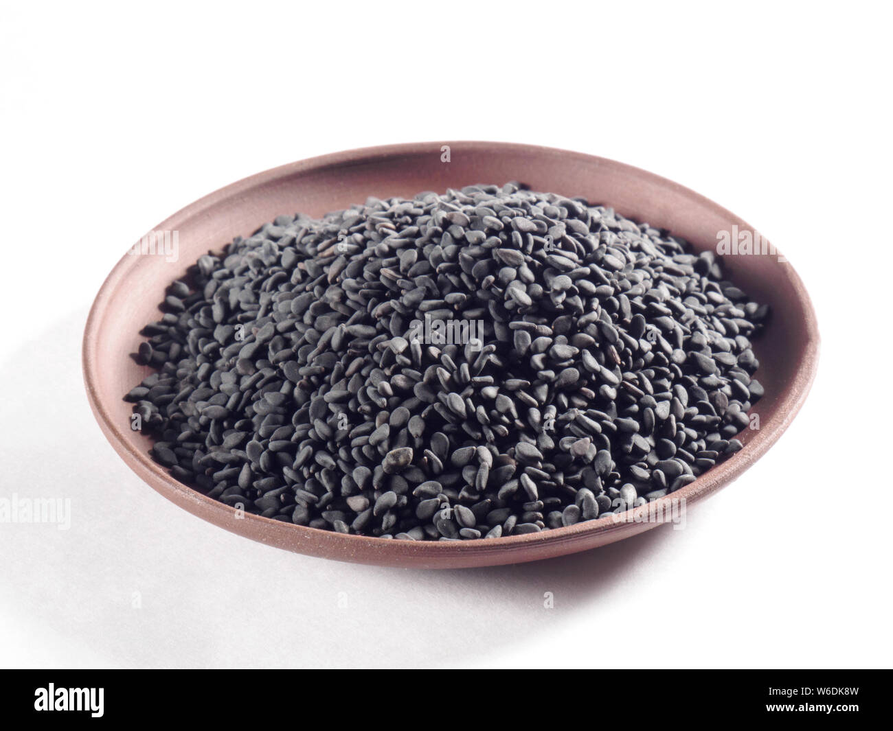Sésame noir (Sesamum indicum) dans une plaque d'argile sur un fond blanc Banque D'Images