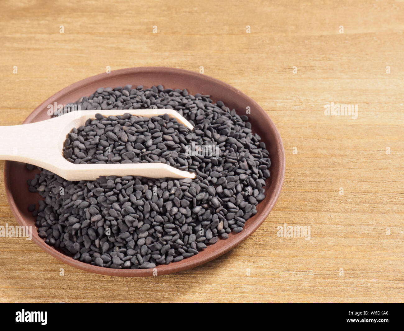 Sésame noir (Sesamum indicum) dans une plaque d'argile avec scoop sur un fond de bois Banque D'Images