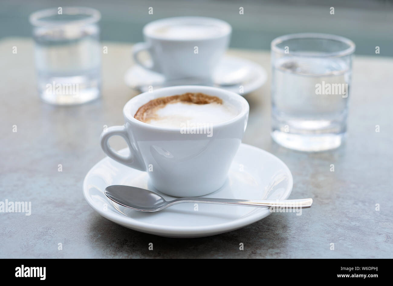 Deux tasses de Cappuccino et deux verres d'eau sur un fond gris texturé. Café de la rue. Close-up. Banque D'Images