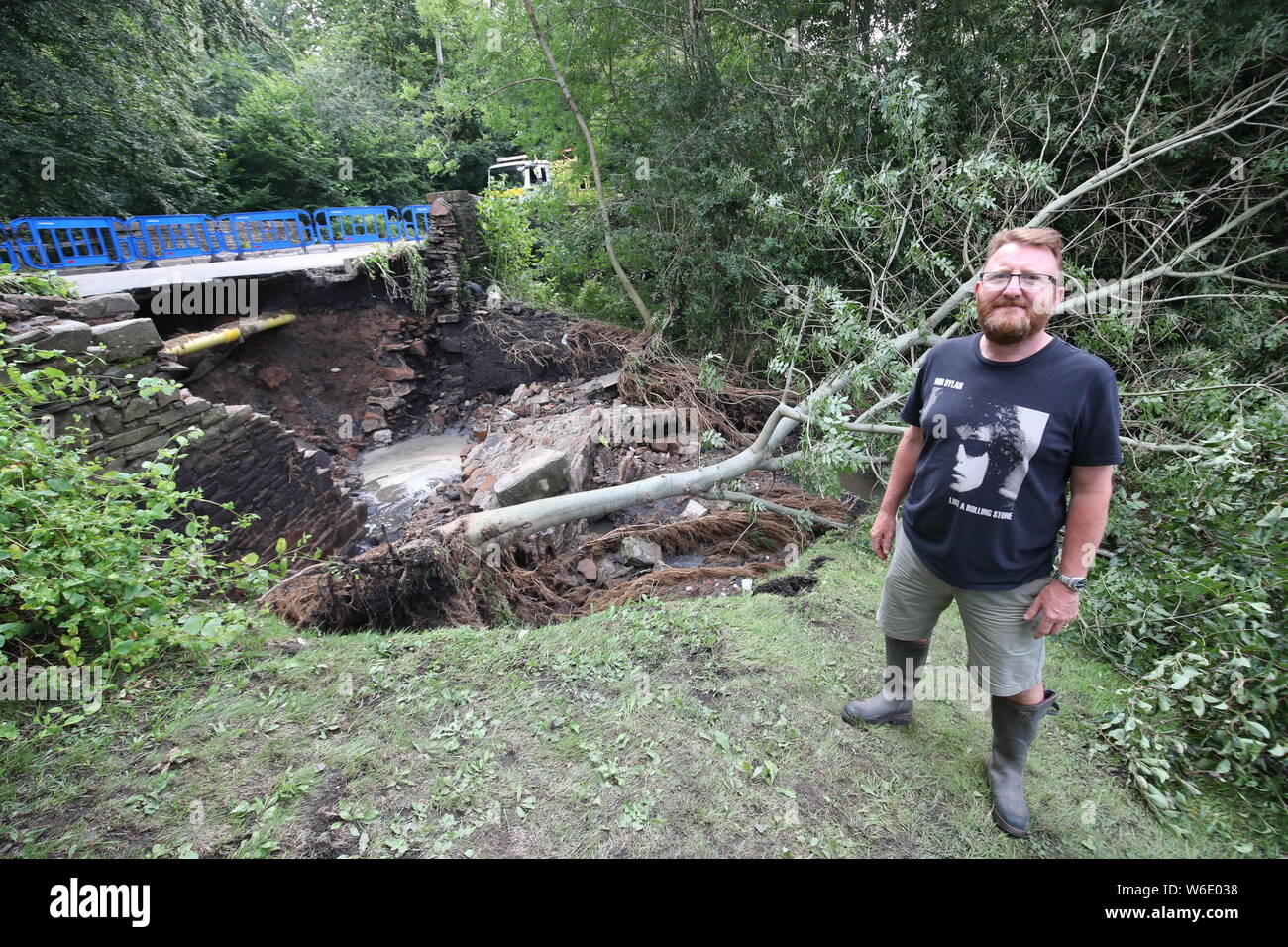 Regardez les travailleurs un pont partiellement effondré en Poynton, Cheshire, où l'inondation a causé un arbre près du pont de tomber dans le jardin de Simon Howcroft (à droite), après de fortes pluies ont causé de graves inondations mercredi. Banque D'Images