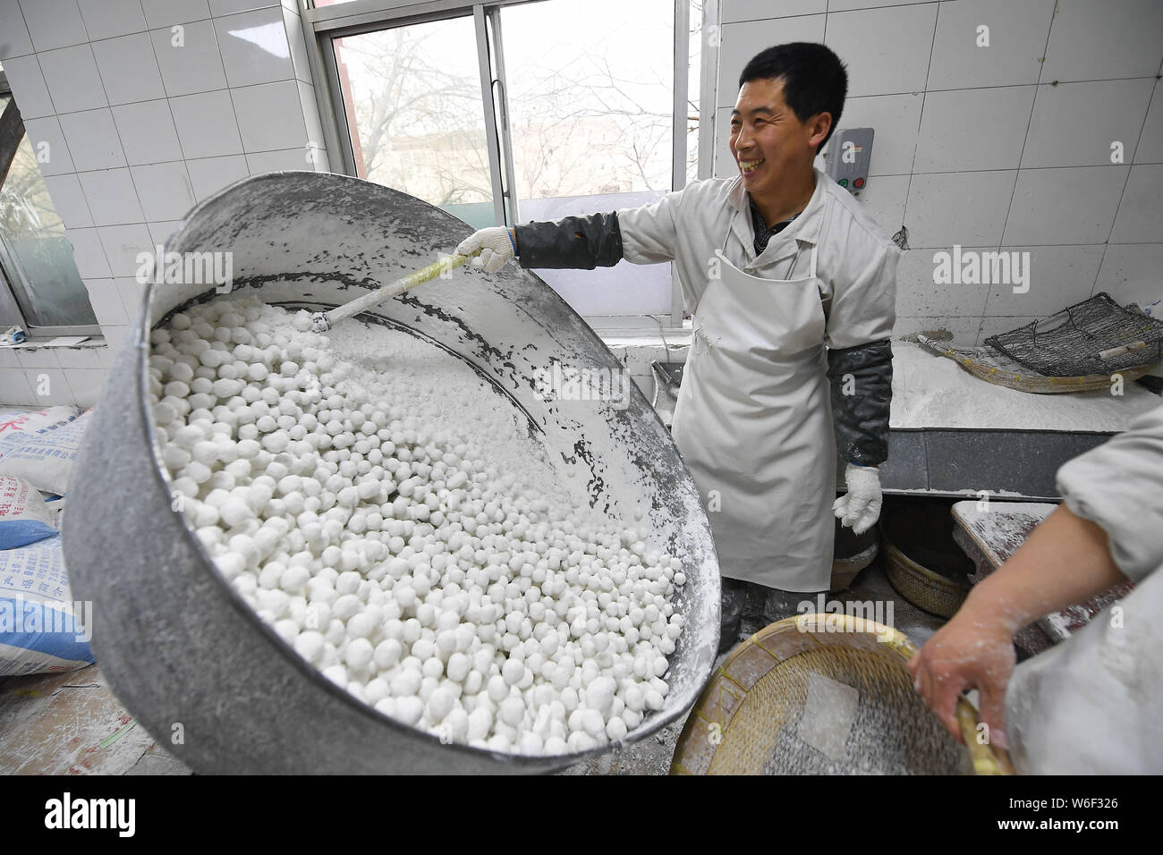 Un travailleur chinois tourbillonne un récipient pour envelopper les farces avec la farine de riz gluant pour faire des boules de riz, également connu sous le nom de Xiao Yuan ou Yuanxiao, à Banque D'Images