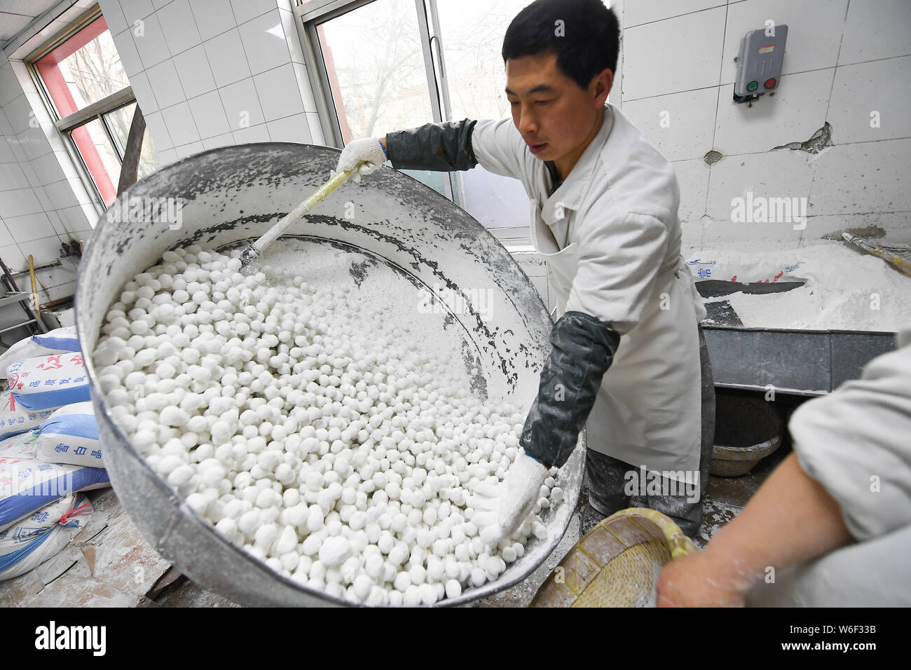 Un travailleur chinois tourbillonne un récipient pour envelopper les farces avec la farine de riz gluant pour faire des boules de riz, également connu sous le nom de Xiao Yuan ou Yuanxiao, à Banque D'Images