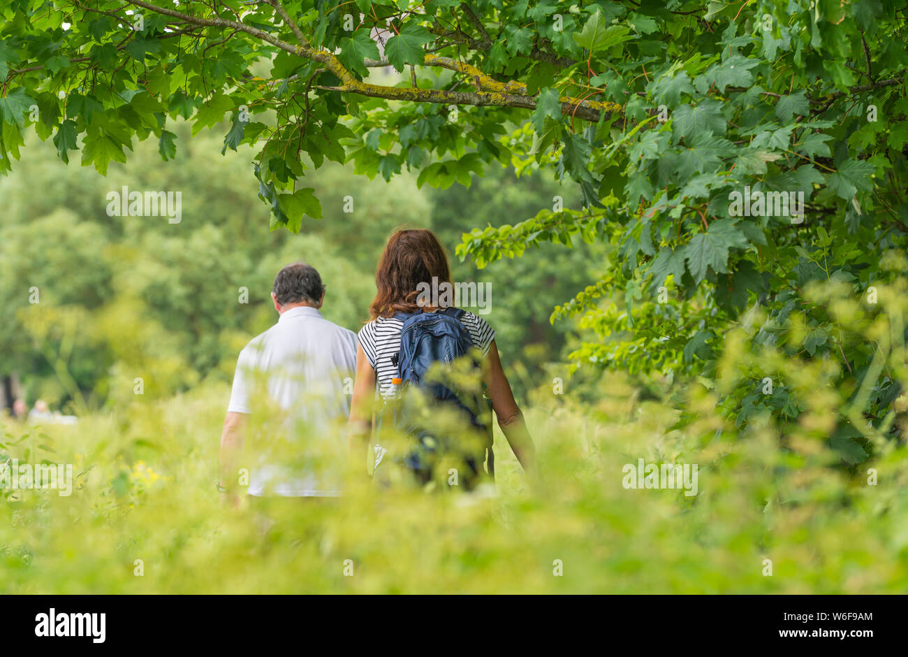 Un couple en train de marcher à travers un chemin de pays en pleine campagne sur une chaude journée de printemps au Royaume-Uni. Banque D'Images