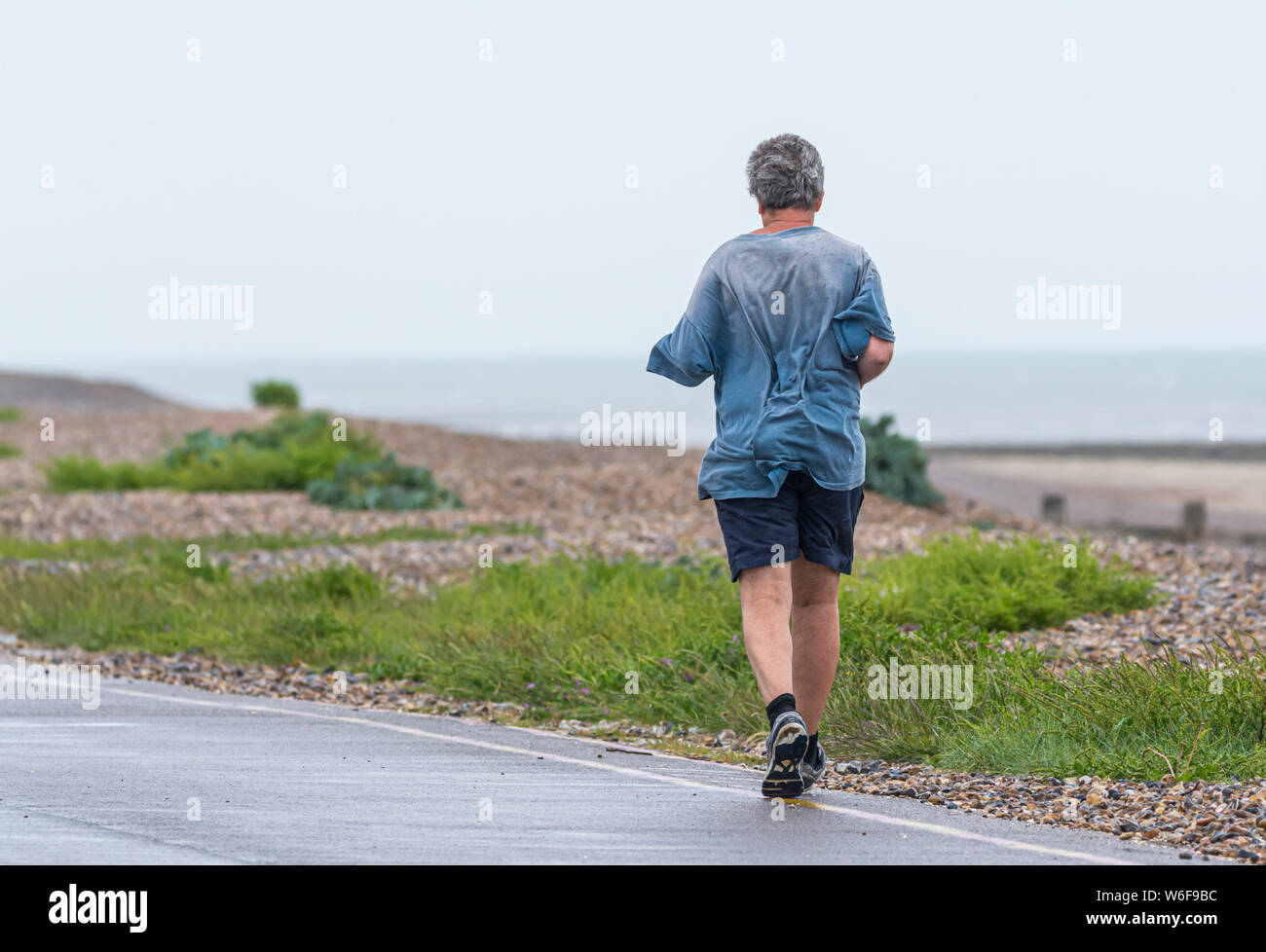 Man jogging le long d'une route en bord de mer sur un mauvais temps pluvieux pendant les jours de pluie. Banque D'Images