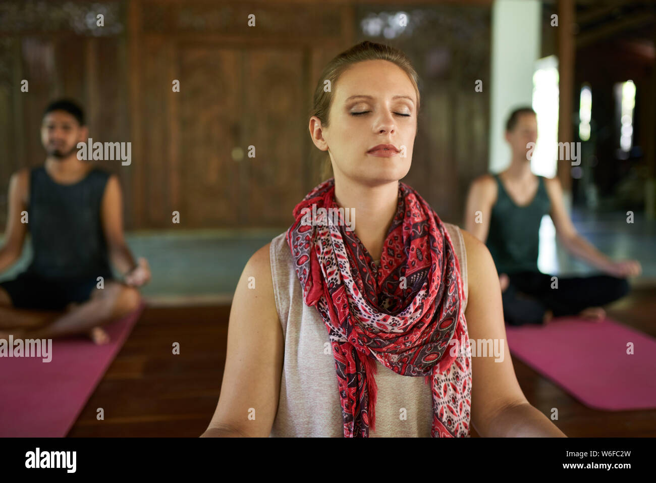 Femme donnant cours de méditation à deux hommes multi-ethnique sur un tapis de yoga dans la région de temple traditionnel à Bali Indonésie Banque D'Images