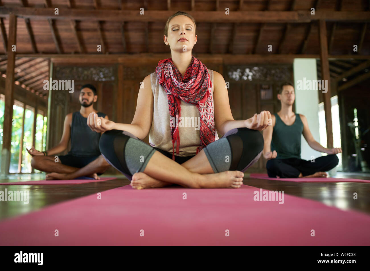 Femme à l'esprit enseigner la méditation à deux hommes multi-ethnique dans lotus poser sur un tapis de yoga dans la région de temple traditionnel à Bali Indonésie Banque D'Images