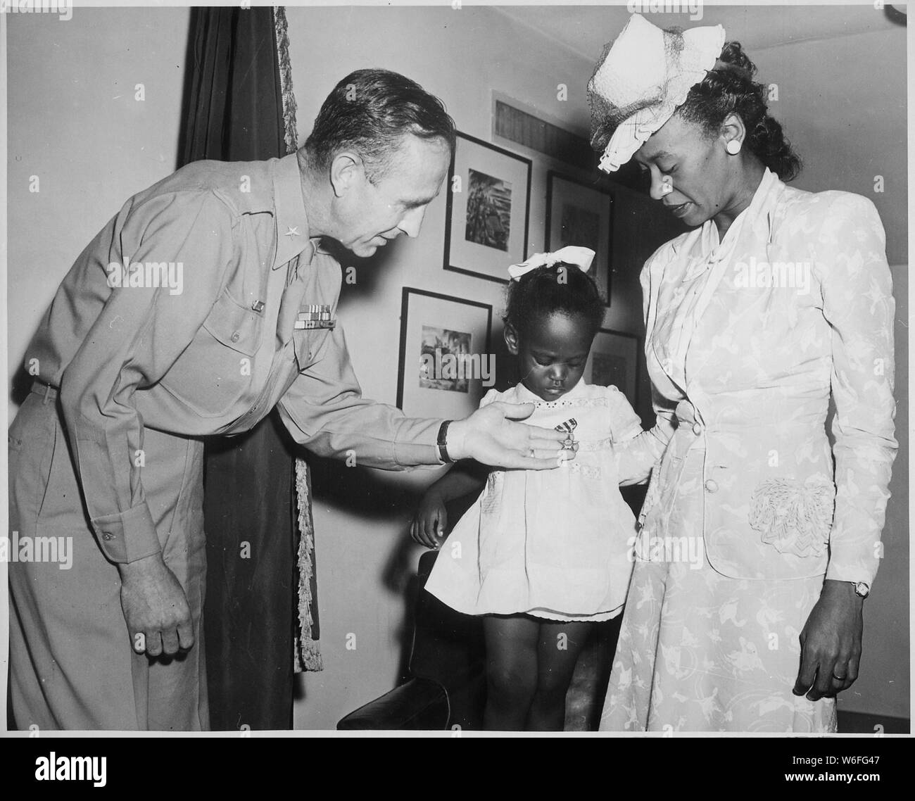 Le brig. Le général Robert N. Young, général commandant du district militaire de Washington, aide Melba Rose, âgés de 2, fille de Mme Rosie L. Madison,...dans l'affichage de la Silver Star à titre posthume, son père 1Le lieutenant John W. Madison, de la 92e Division d'infanterie, qui a été tué dans l'action en Italie..., ca. 1941 - ca. 1945 Banque D'Images