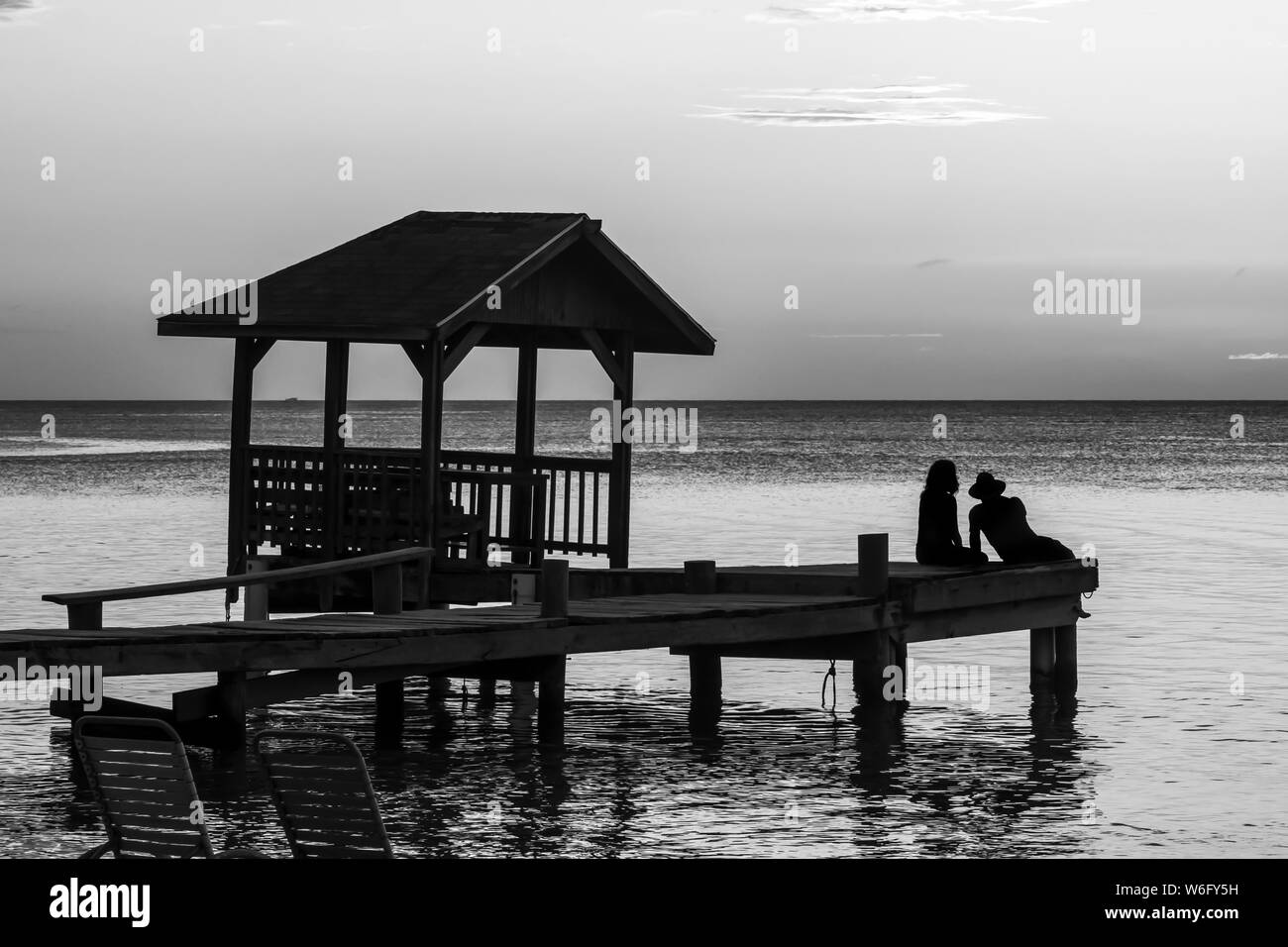 Un couple se trouve au bout d'un quai donnant sur l'océan tranquille au coucher du soleil ; Roatan, Bay Islands Department, Honduras Banque D'Images