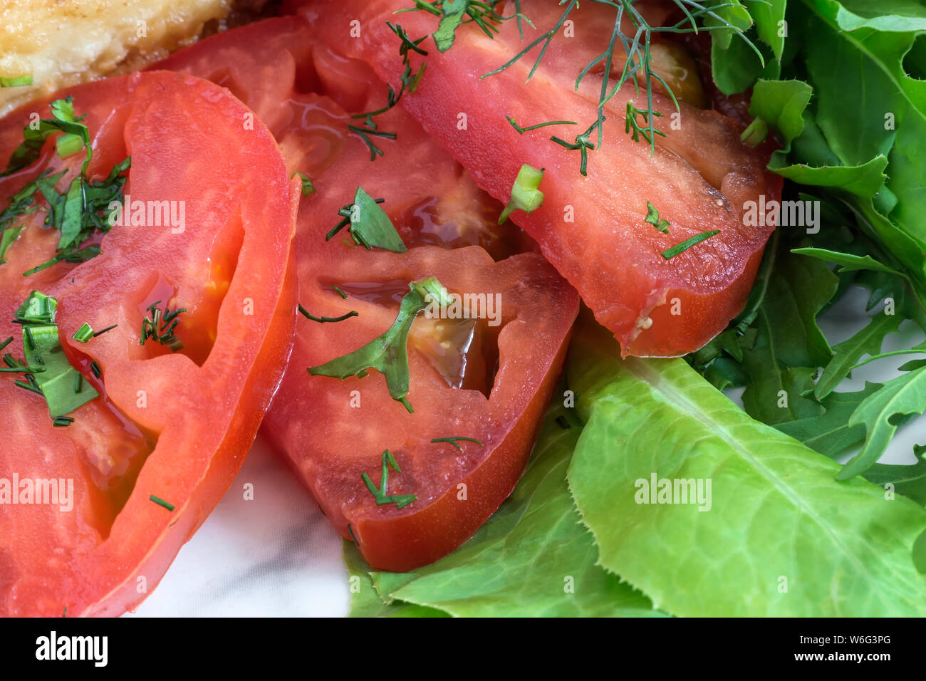 Sur une plaque trois tranches de tomates rouges mûres à côté d'une salade verte et le persil. Présenté en gros plan. Banque D'Images