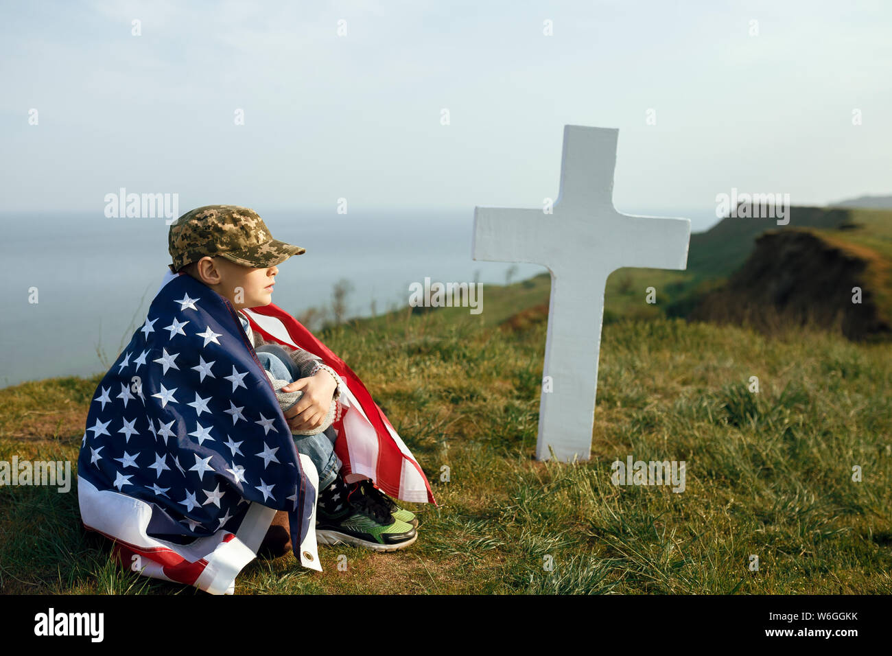 Un jeune garçon dans un chapeau militaire, couverts par le drapeau de l'united states assis sur la tombe de son défunt père. 27 mai Memorial Day Banque D'Images