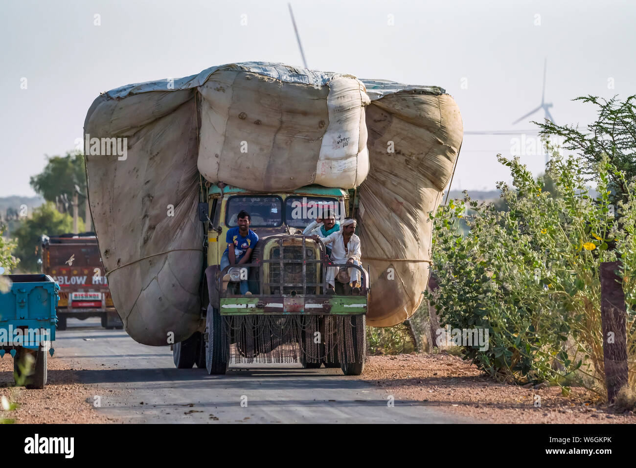 Camion transportant une énorme charge de blé dans le Nord de l'Inde avec trois hommes à cheval sur l'avant du chariot ; Rajasthan, Inde Banque D'Images