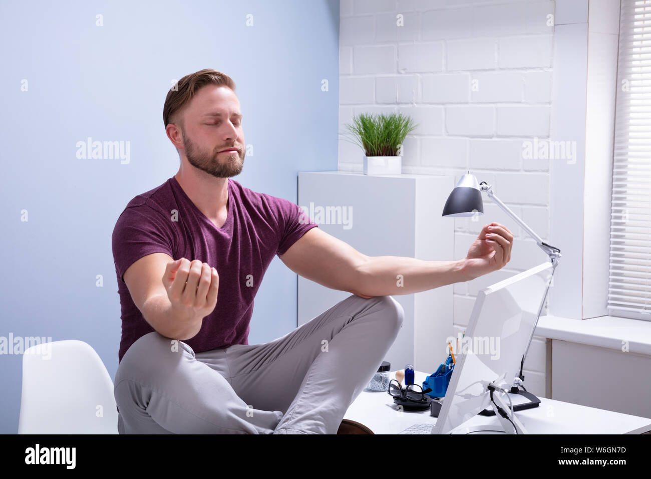 Young Businessman Sitting on Desk In Office Banque D'Images