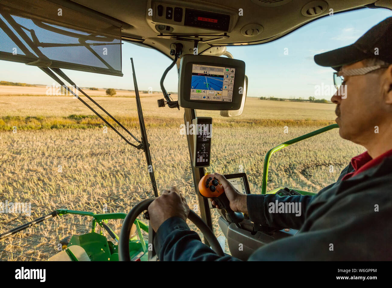 Un agriculteur dans la cabine de son combiner la récolte du canola au coucher du soleil et à l'aide de l'automatisation informatique dans son équipement ; Legal, Alberta, Canada Banque D'Images