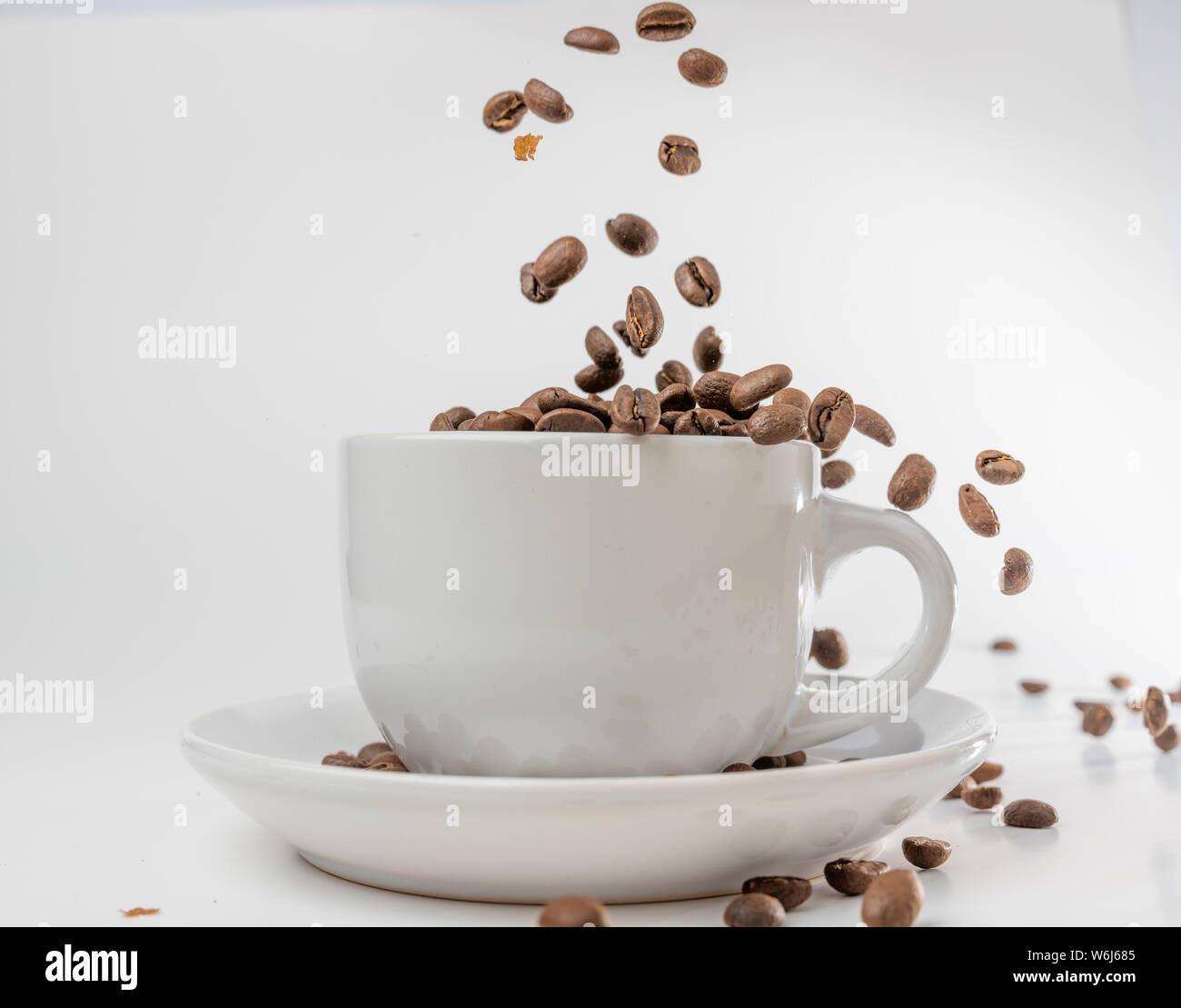 Café en grains tombent dans une tasse et soucoupe en porcelaine blanche, bondissant et sautant à travers l'air alerte transport l'excitation, toutes isolées contre un blanc Banque D'Images