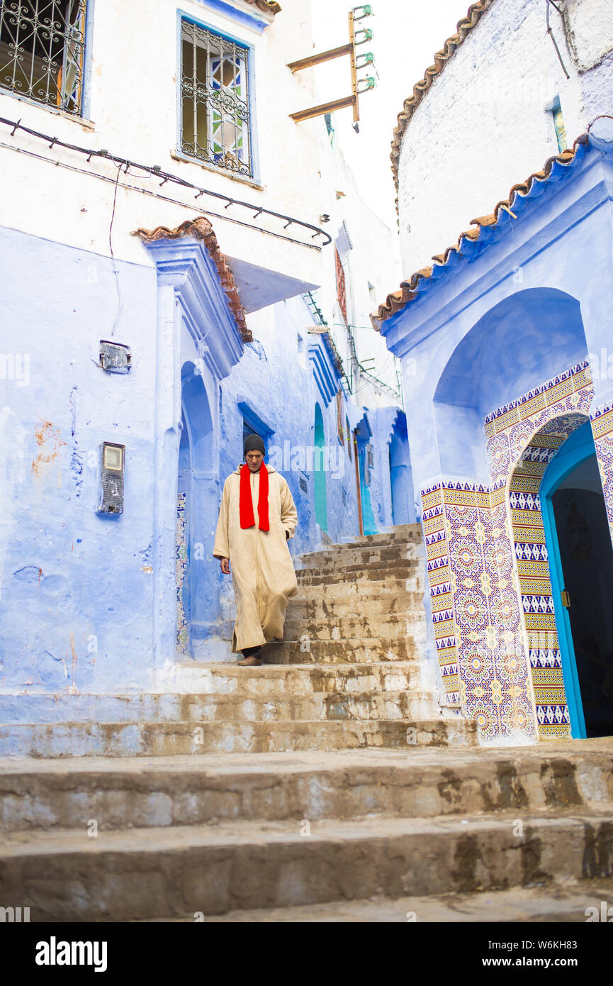 Un vieil homme, vêtu de la traditionnelle marche est Djellabah par l'étroite ruelle de Chefchaouen, Maroc. Banque D'Images