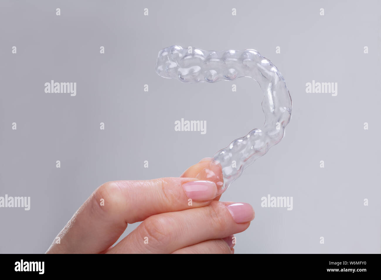 Close-up of Woman's Hand Holding accolades en plastique transparent sur fond gris Banque D'Images