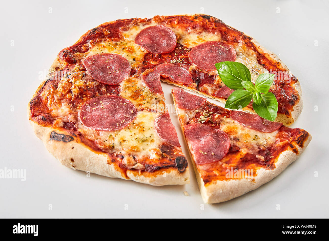 Tranches de salami italien pizza garnie de basilic frais sur un fond blanc pour la publicité ou un menu Banque D'Images