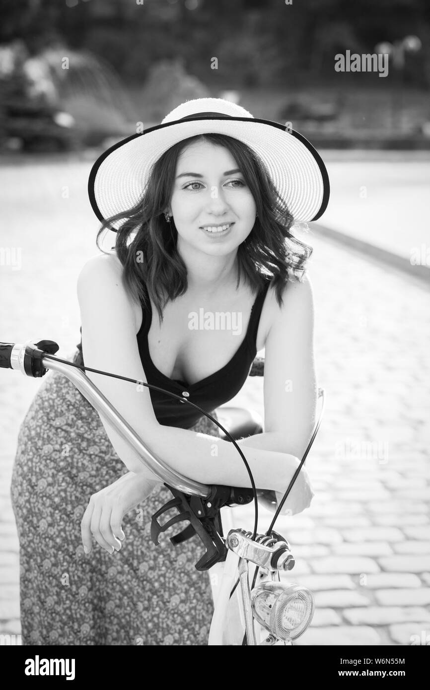 Young woman in hat les cheveux bouclés et dress posing avec moto à la vieille ville européenne, l'heure du coucher du soleil, à côté, souriant, monochrome Banque D'Images