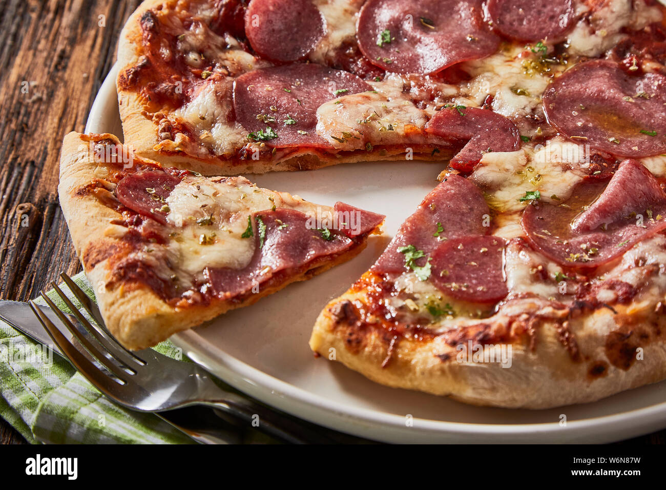 Pizza salami italien régional savoureux avec des herbes sont tranchés et servi sur une plaque blanche générique dans un close up portrait Banque D'Images