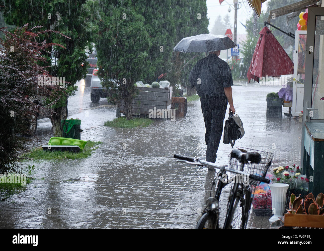 Homme avec porte-documents marcher sous la pluie avec un parapluie. La création de pluie de flaques sur trottoir massive Banque D'Images