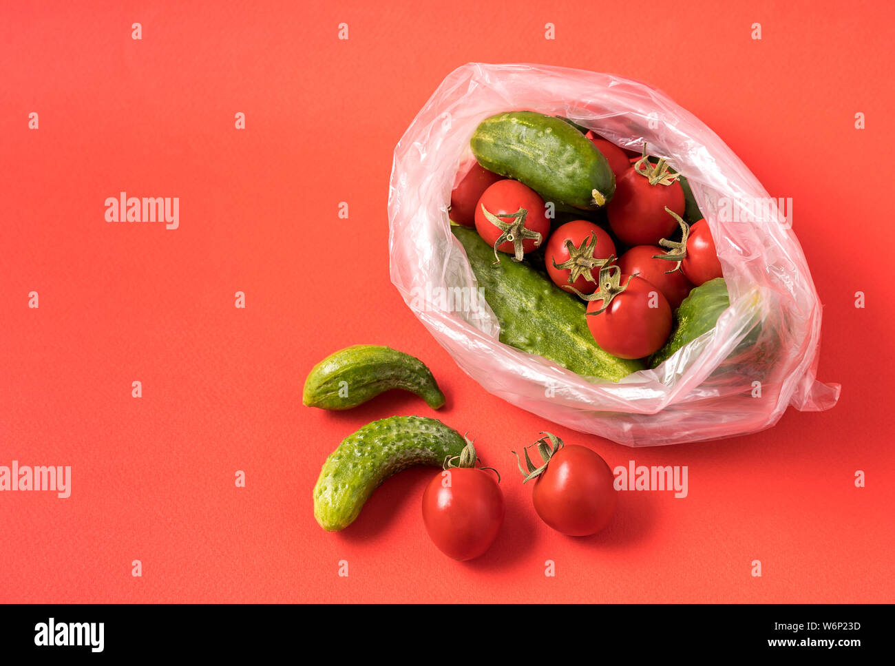 Vue de face des concombres et des tomates dans un sac plastique sur fond rouge. Image montre le harmness à l'aide de sacs de stockage de l'alimentation artificielle. Banque D'Images