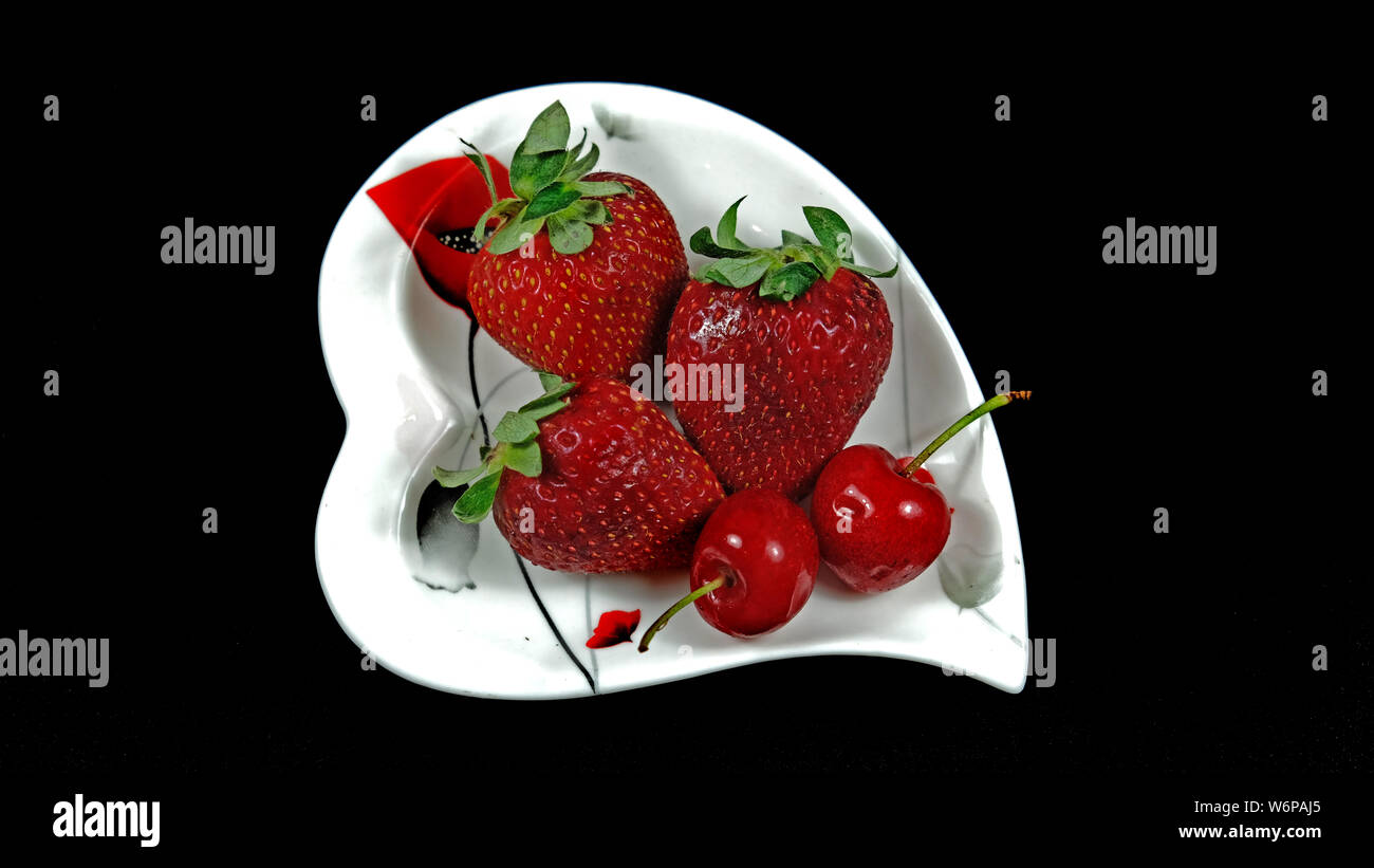 Les cerises et les fraises sur la plaque coeur Banque D'Images