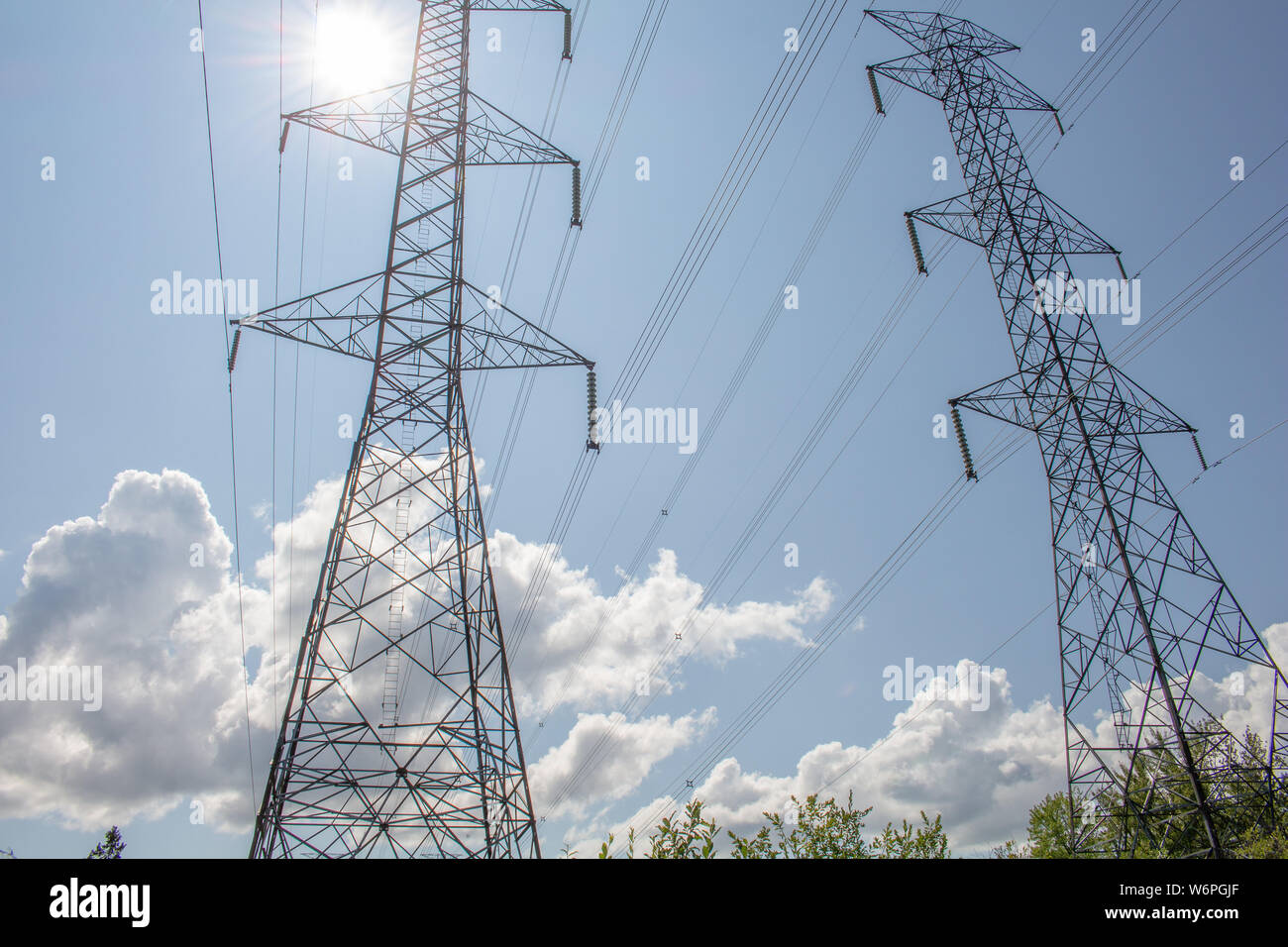 Une paire de tours de transmission électriques câbles et suspendre debout contre un ciel bleu, avec le soleil qui brille à travers de l'arrière. Banque D'Images