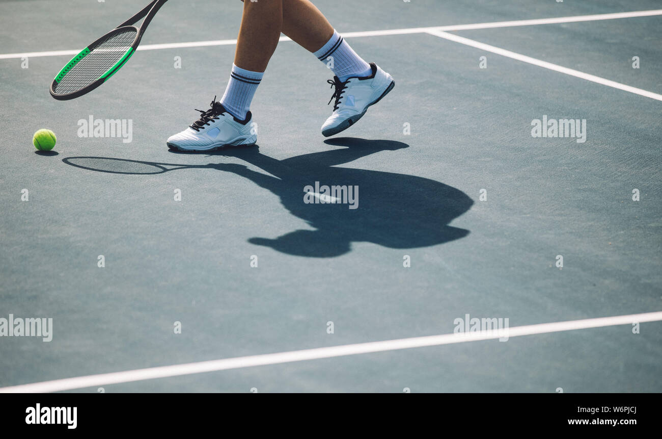 Cropped shot de sportif sur un court de tennis. Joueur de tennis sur surface dure de flexion avec raquette pour aller chercher la balle. Banque D'Images