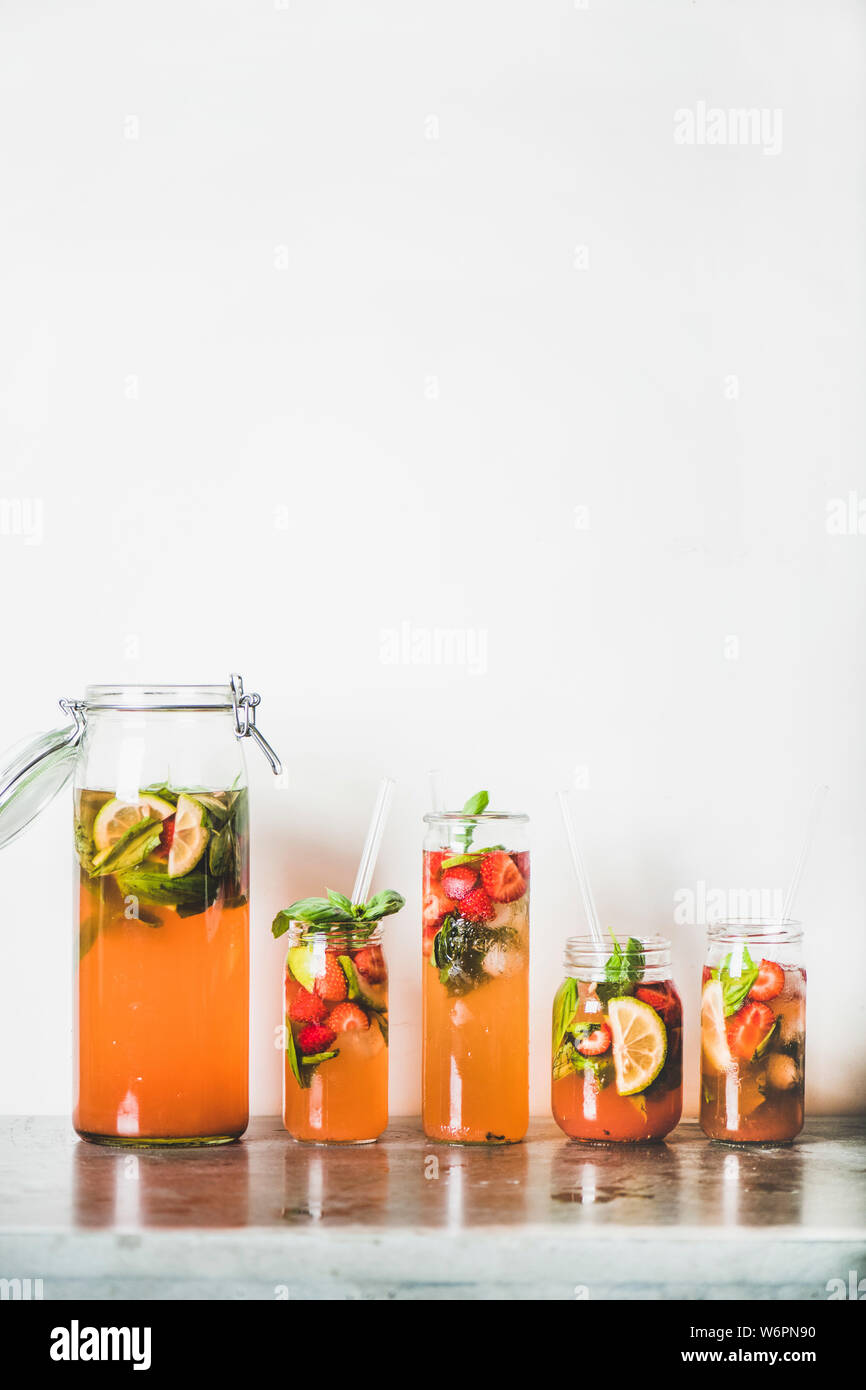 Fraise et basilic fait maison ou Limonade Thé glacé dans le verre et sans poignée avec l'éco-friendly plastique pailles sur table béton gris, blanc mur à ba Banque D'Images