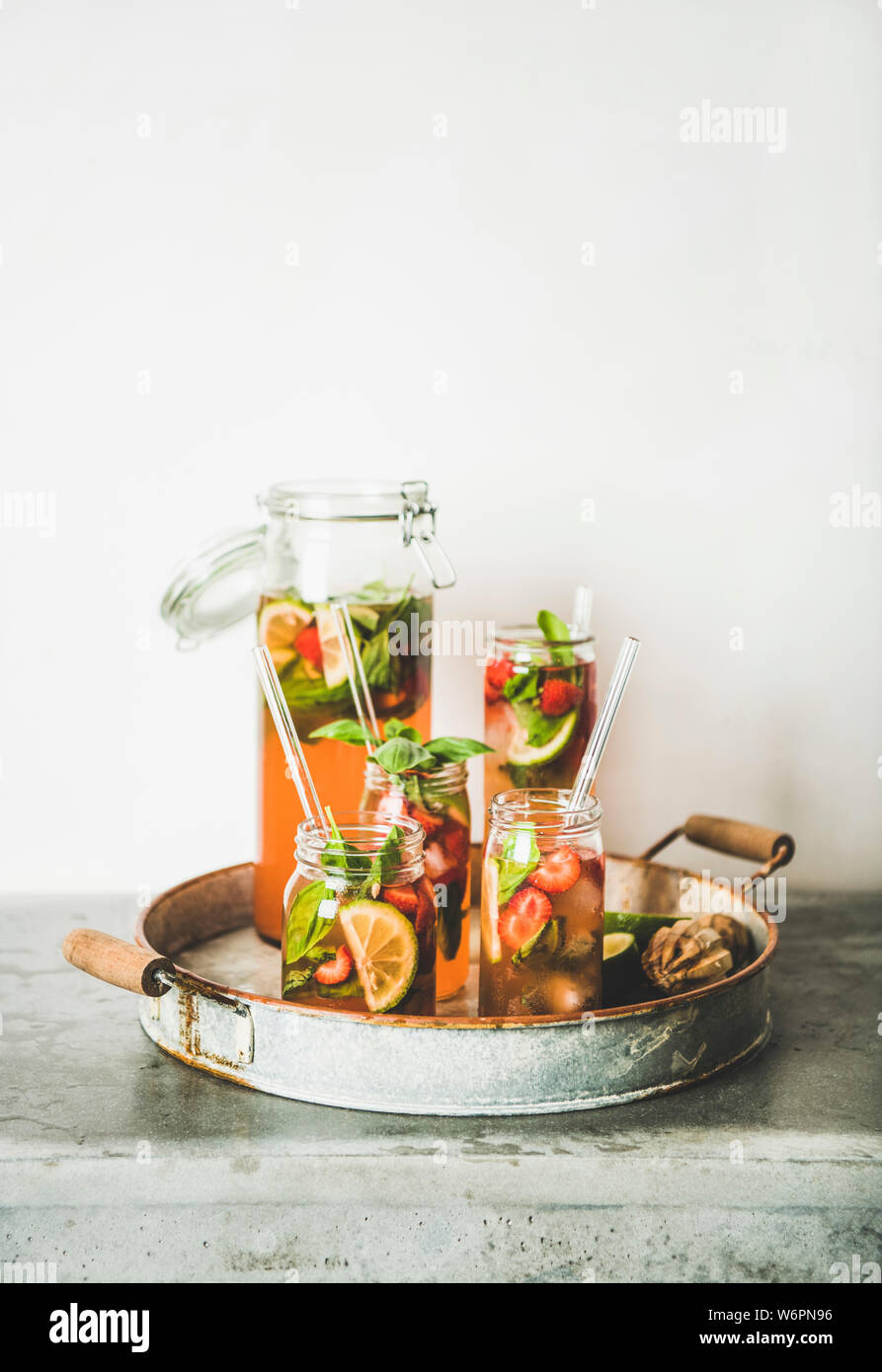 Fraise et basilic fait maison ou Limonade Thé glacé dans des bocaux en verre avec eco-friendly pailles plastique sur le plateau métallique rustique, mur blanc au fond, Banque D'Images