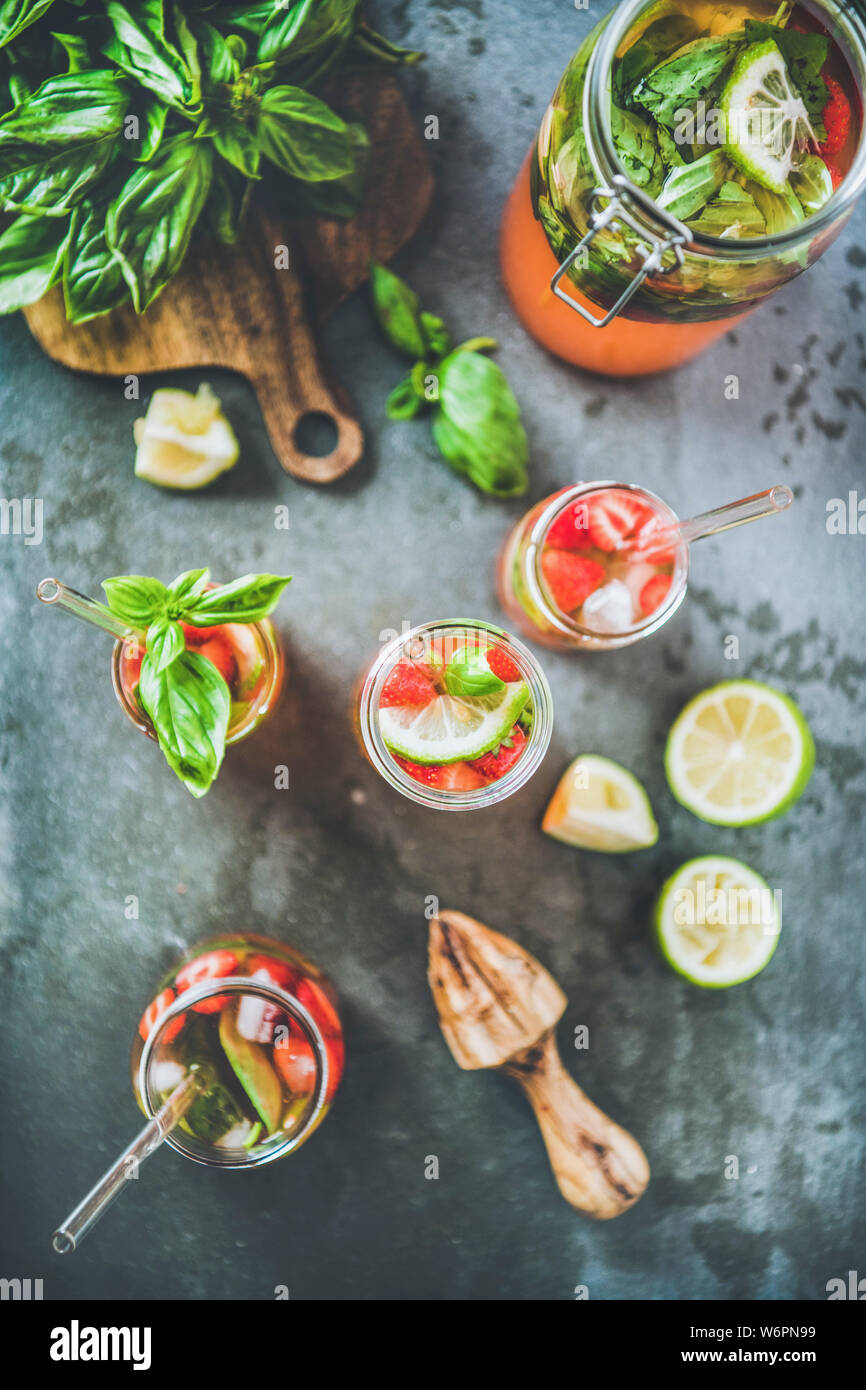 Des fraises fraîches de basilic et glace limonade ou plateau en verre double paroi avec eco-friendly plastique pailles et les ingrédients sur le tableau b gris foncé Banque D'Images