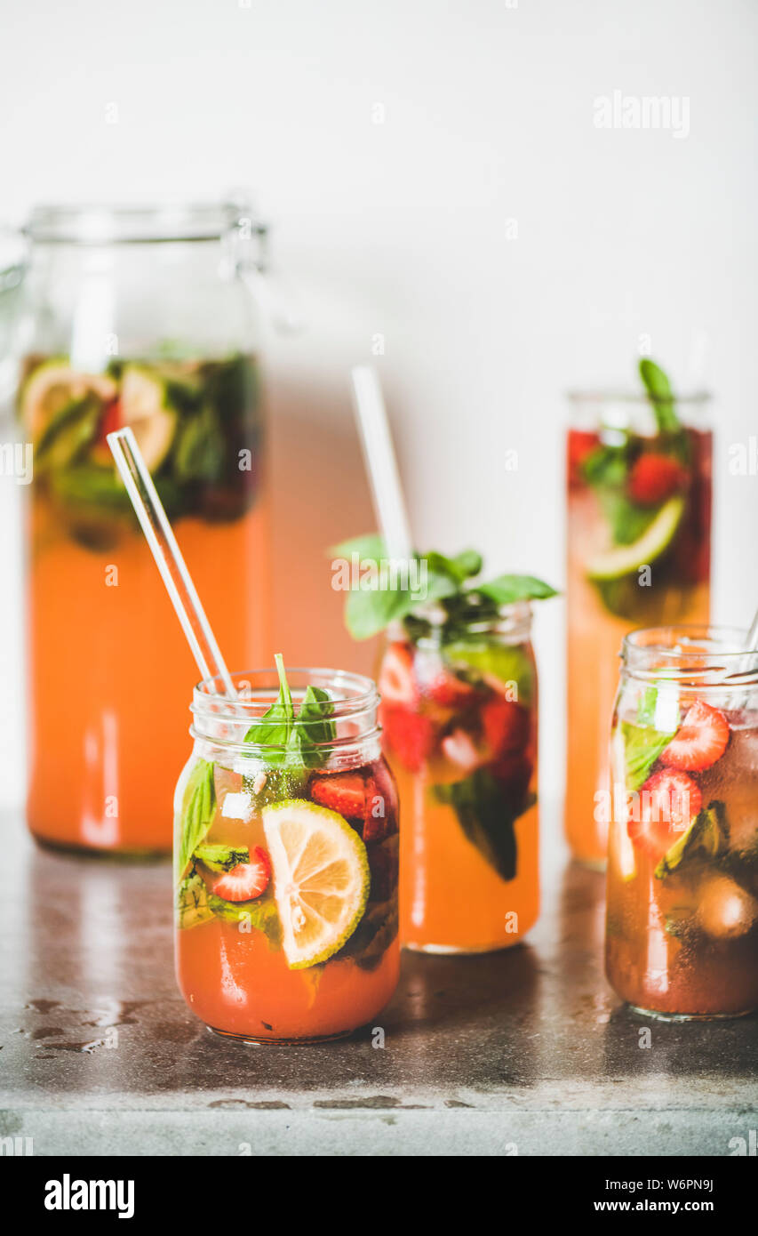 Fraise et basilic fait maison ou Limonade Thé glacé dans le verre sans poignée avec eco-friendly plastique pailles sur table béton gris, blanc mur à zone Banque D'Images