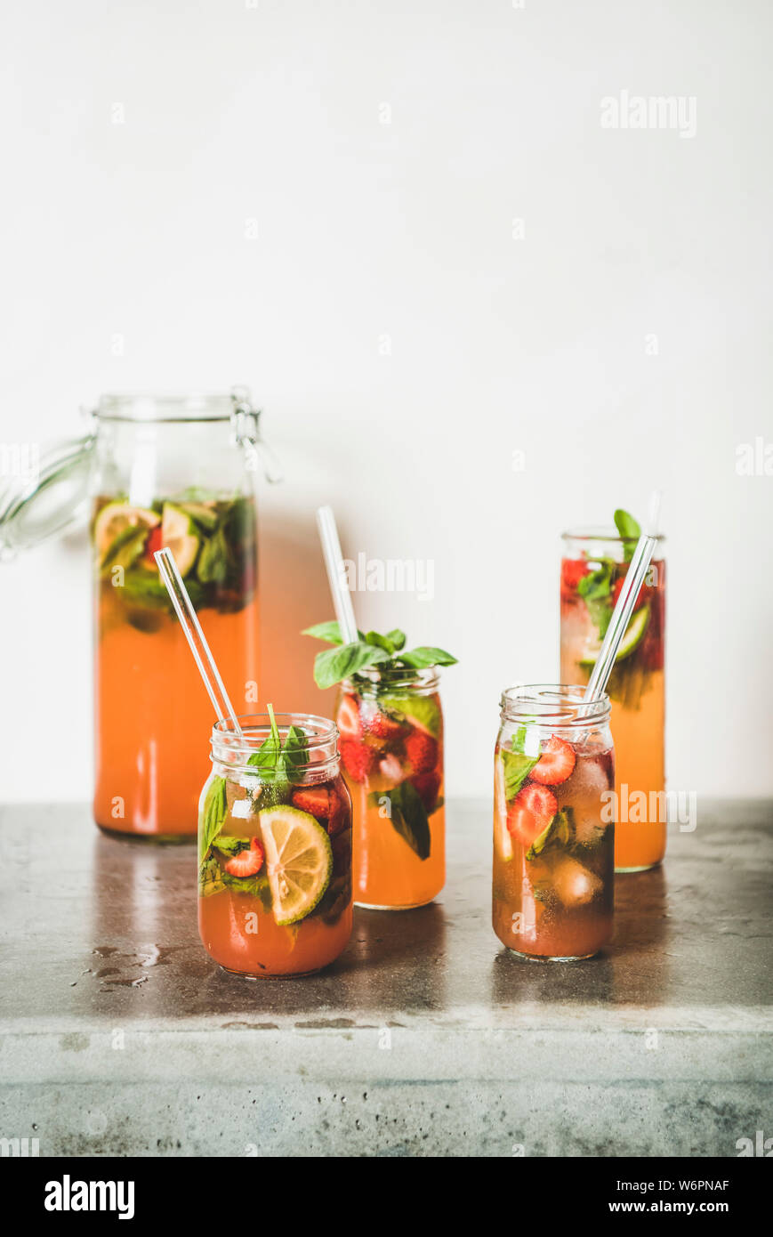 Fraise et basilic fait maison ou Limonade Thé glacé dans le verre sans poignée avec eco-friendly plastique pailles sur table béton gris, blanc mur à zone Banque D'Images