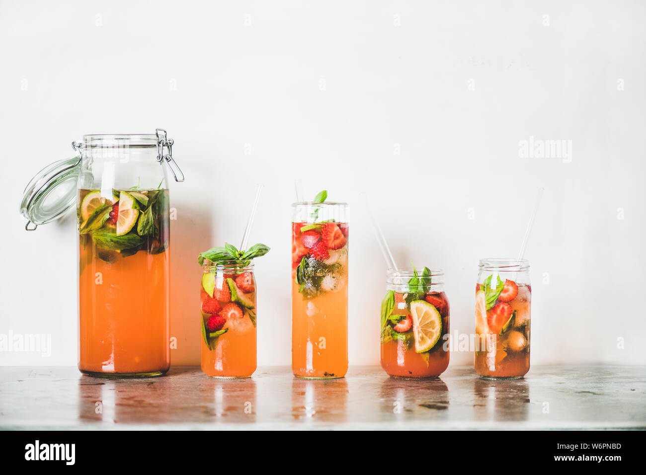 Fraise et basilic fait maison ou Limonade Thé glacé dans le verre sans poignée avec eco-friendly plastique pailles sur table béton gris, blanc mur à zone Banque D'Images