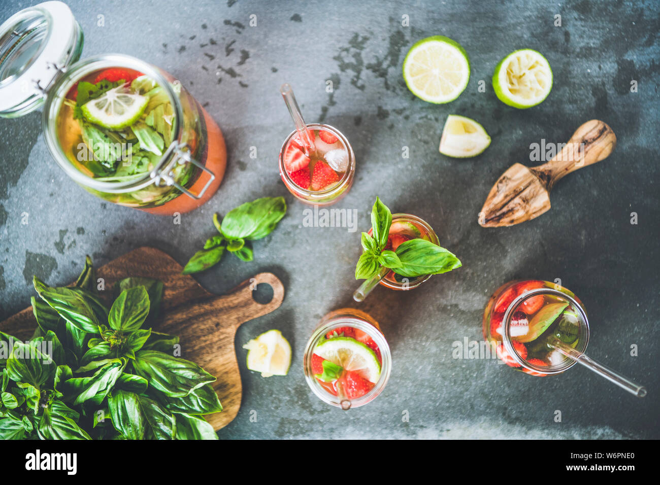 Des fraises fraîches et basilic ou Limonade Thé glacé- dans le verre sans poignée avec eco-friendly plastique pailles et d'ingrédients frais sur gris foncé Banque D'Images