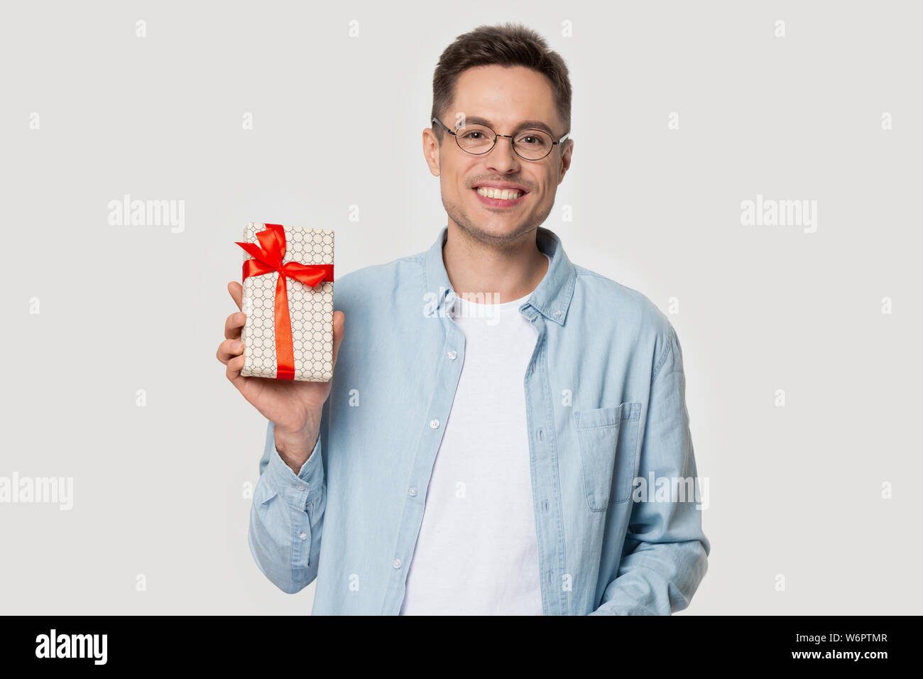 Heureux jeune homme poser sur fond gris studio holding gift box Banque D'Images