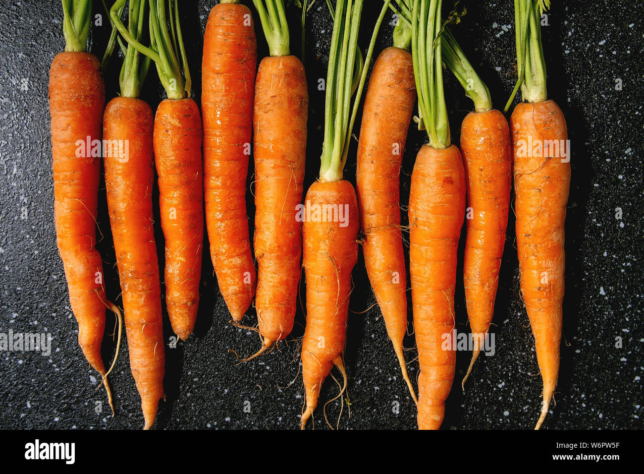 Les jeunes avec des dessus de carotte dans la rangée sur noir texture background. Mise à plat, de l'espace. Concept de cuisine, de l'alimentation arrière-plan. Banque D'Images