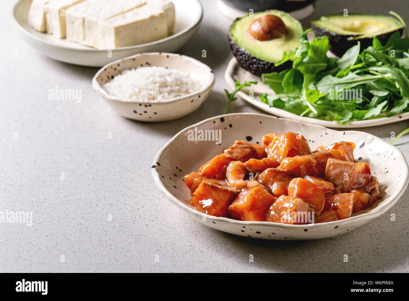 Ingrédients pour la cuisson avec le bol. Le riz, la sauce soja saumon mariné, avocat, fromage de tofu et salade verte dans des bols en céramique gris repéré sur table. Banque D'Images