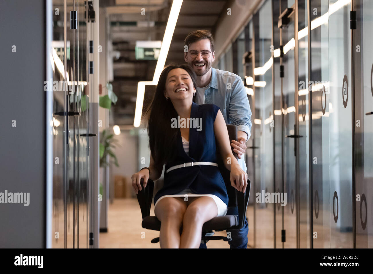 Deux heureux collègues ayant l'amusement ride on chair in office Banque D'Images